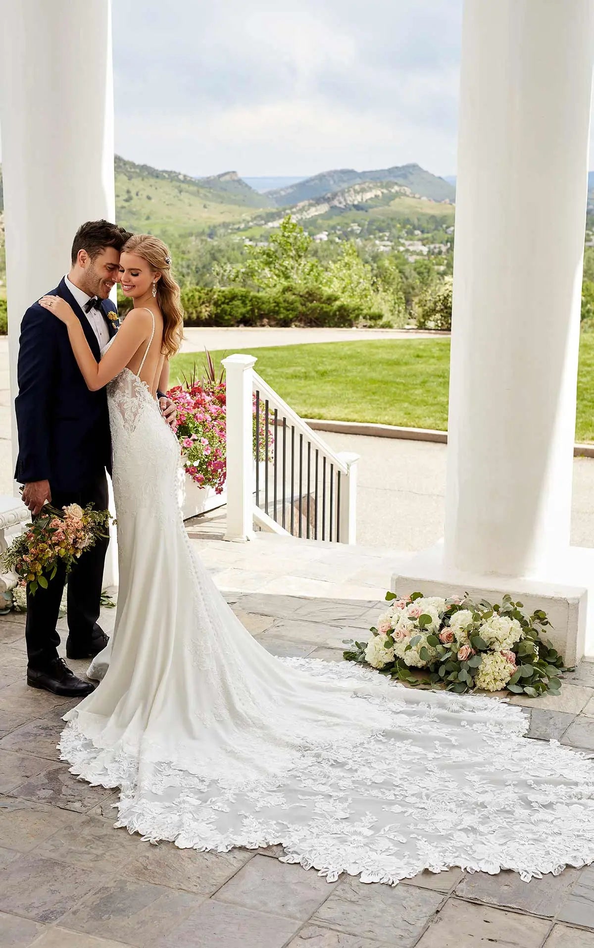 Couple in wedding attire standing on a stone pathway with a scenic background