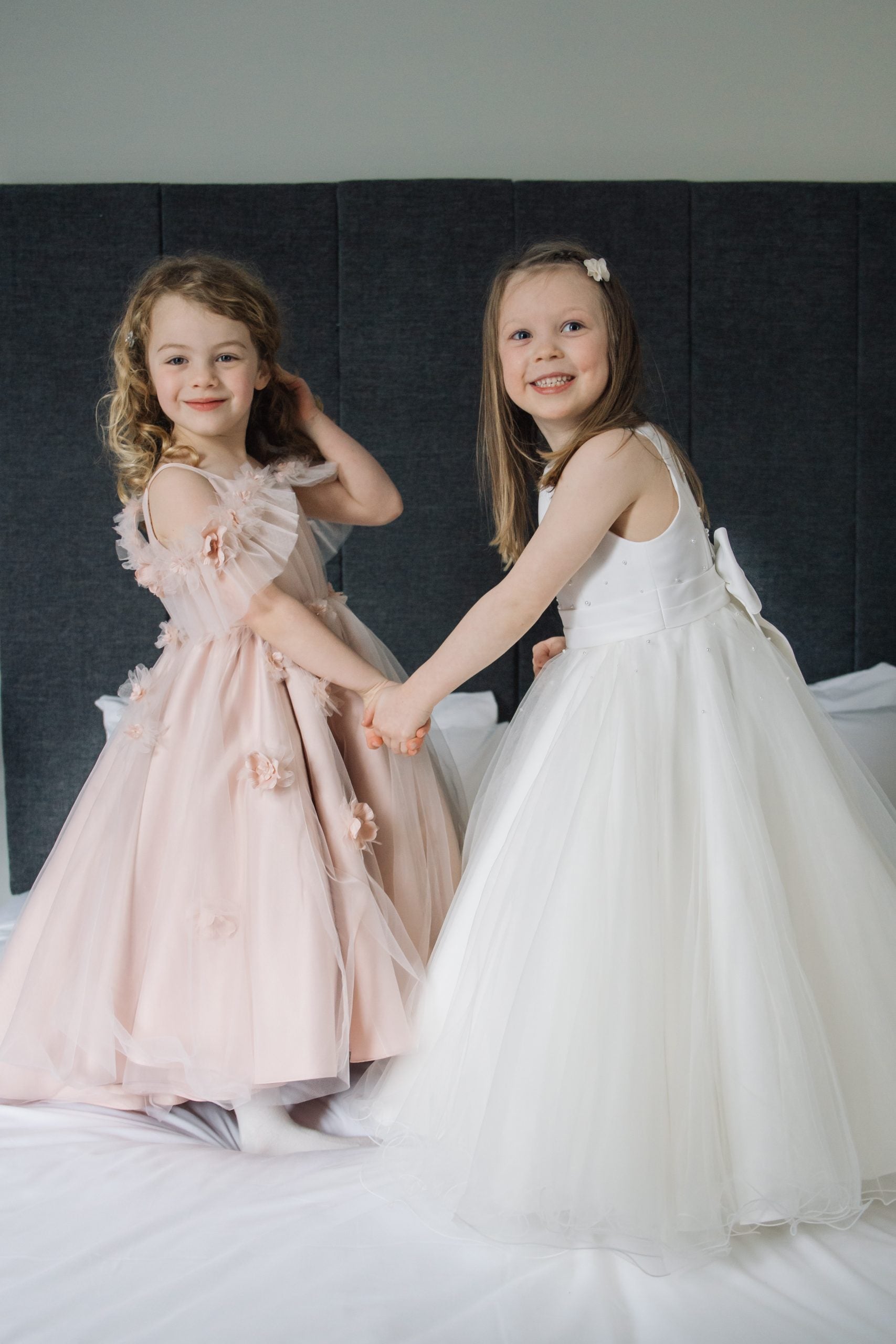 Two young girls in formal dresses holding hands against a plain background